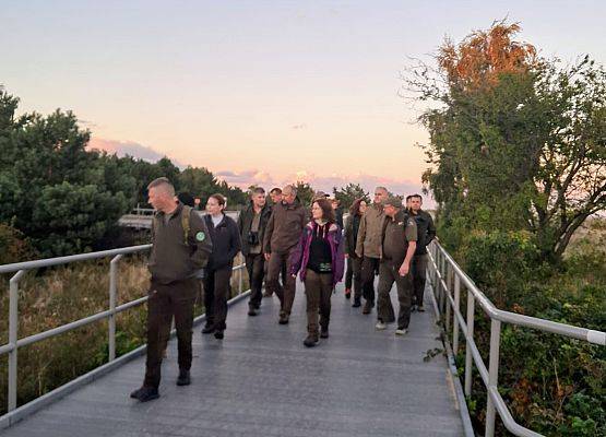 Konferencja INVENT 2025 grupa ludzi idących na kładce, w tle zachodzące słońce