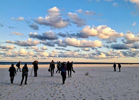 Konferencja INVENT 2025 Na plaży widać grupę osób spacerujących, otoczonych piaskiem i falami.