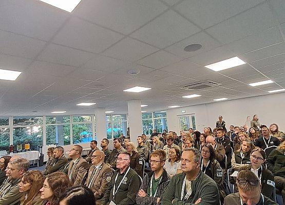 Konferencja Grupa osób siedzi w pomieszczeniu, skupiona na prezentacji lub dyskusji.